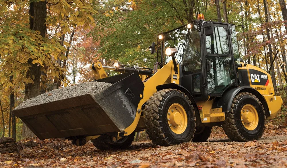 CAT 906M wheel loader carrying gravel in a forested worksite in Seattle, Washington.