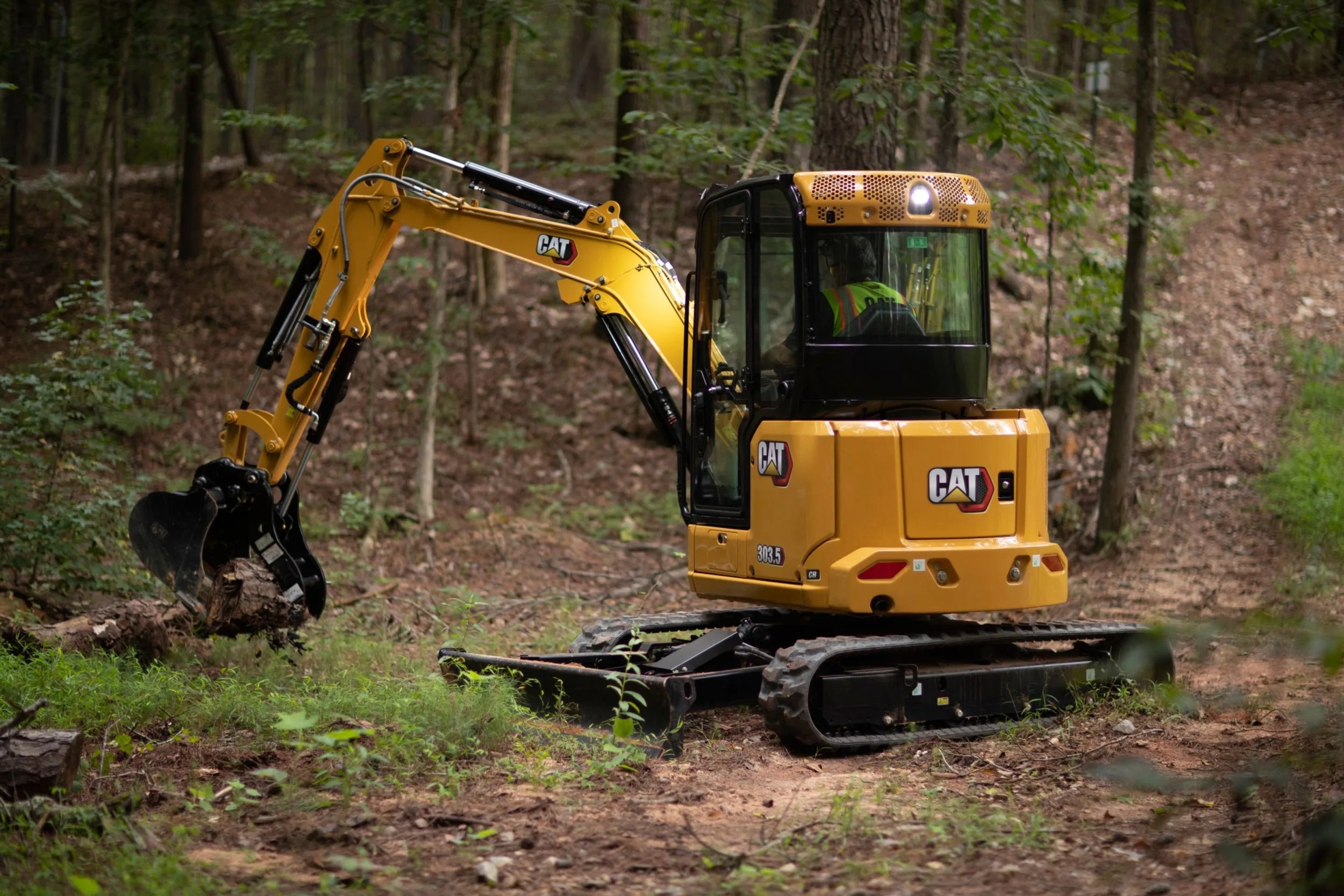 Cat® 303.5 mini hydraulic excavator at work in a wooded construction site, representing high-performance excavator rental in Seattle for diverse project needs.
