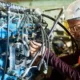 Technician inspecting hydraulic control system in heavy construction equipment for maintenance, at Williams Diesel LLC site in Seattle, Washington.