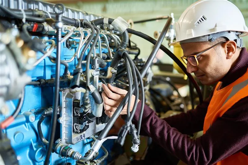 Technician inspecting hydraulic control system in heavy construction equipment for maintenance, at Williams Diesel LLC site in Seattle, Washington.