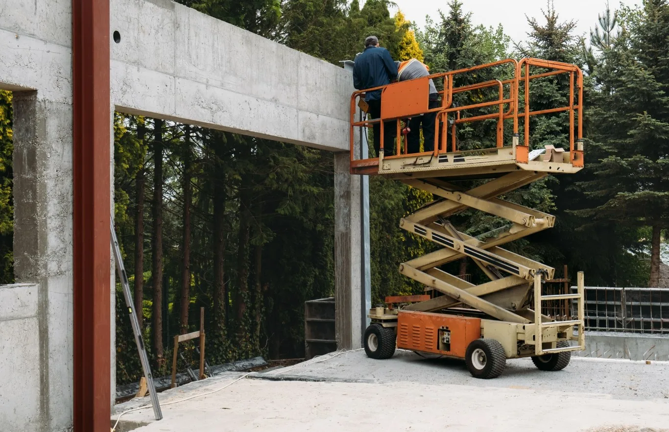 Construction workers operating a 25 ft scissor lift at a job site surrounded by trees, representing a reliable 25 ft scissor lift rental in Seattle offered by Williams Diesel LLC