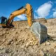 Mini excavator rental in Seattle being used at a construction site, showcasing the equipment's efficiency and digging capabilities on rugged terrain under a clear blue sky.