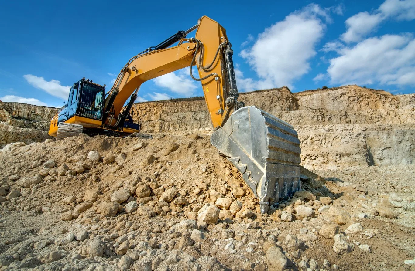 Mini excavator rental in Seattle being used at a construction site, showcasing the equipment's efficiency and digging capabilities on rugged terrain under a clear blue sky.