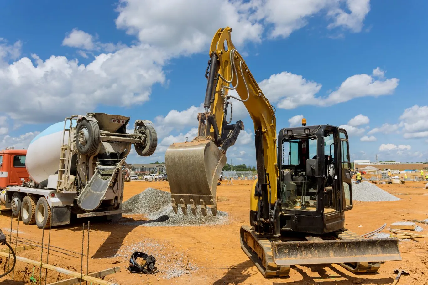 Construction equipment rental in Seattle with a compact excavator and cement truck working on a building site under a clear sky.