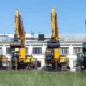 A lineup of heavy construction excavators parked outside a warehouse, representing a local equipment rental company offering reliable machinery for construction and excavation projects.