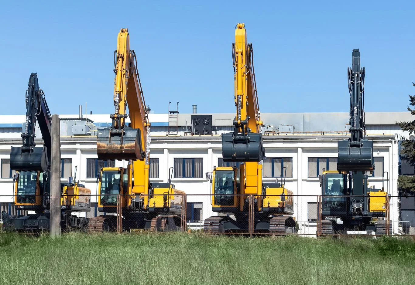 A lineup of heavy construction excavators parked outside a warehouse, representing a local equipment rental company offering reliable machinery for construction and excavation projects.
