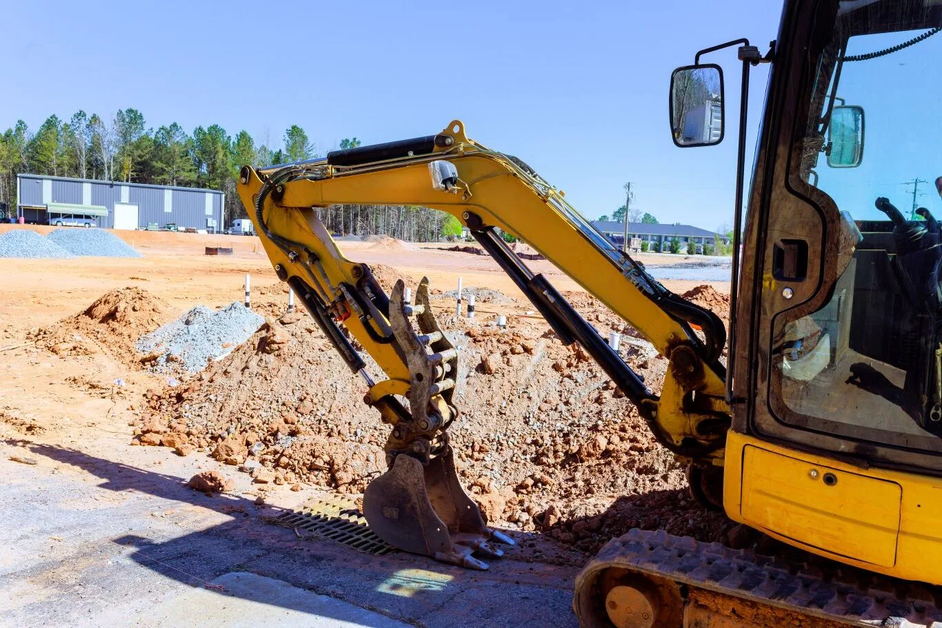 Yellow construction equipment at a worksite showing a digging arm used for mini excavator attachments rental services.