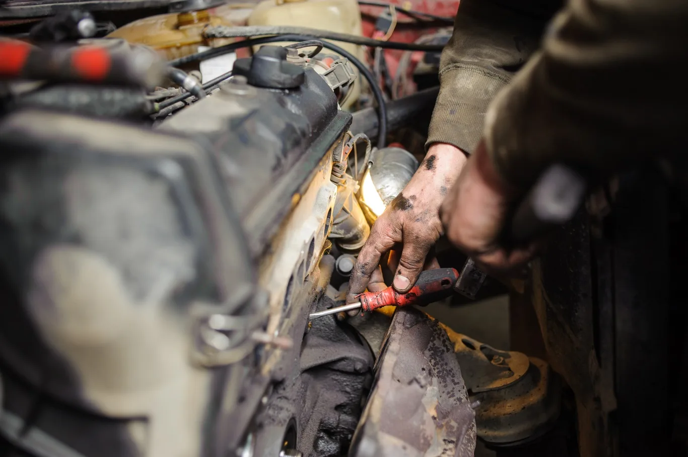A mechanic performing emergency diesel repair on a truck engine, working with tools under dim lighting to fix a critical issue.