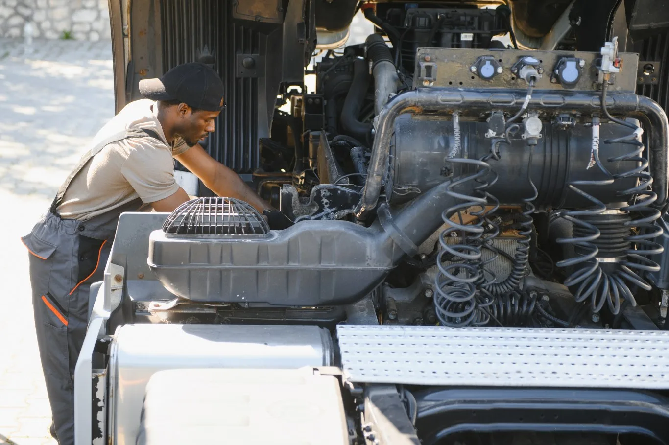 A technician performing heavy equipment repair on a large diesel machine, inspecting engine components and mechanical parts outdoors.