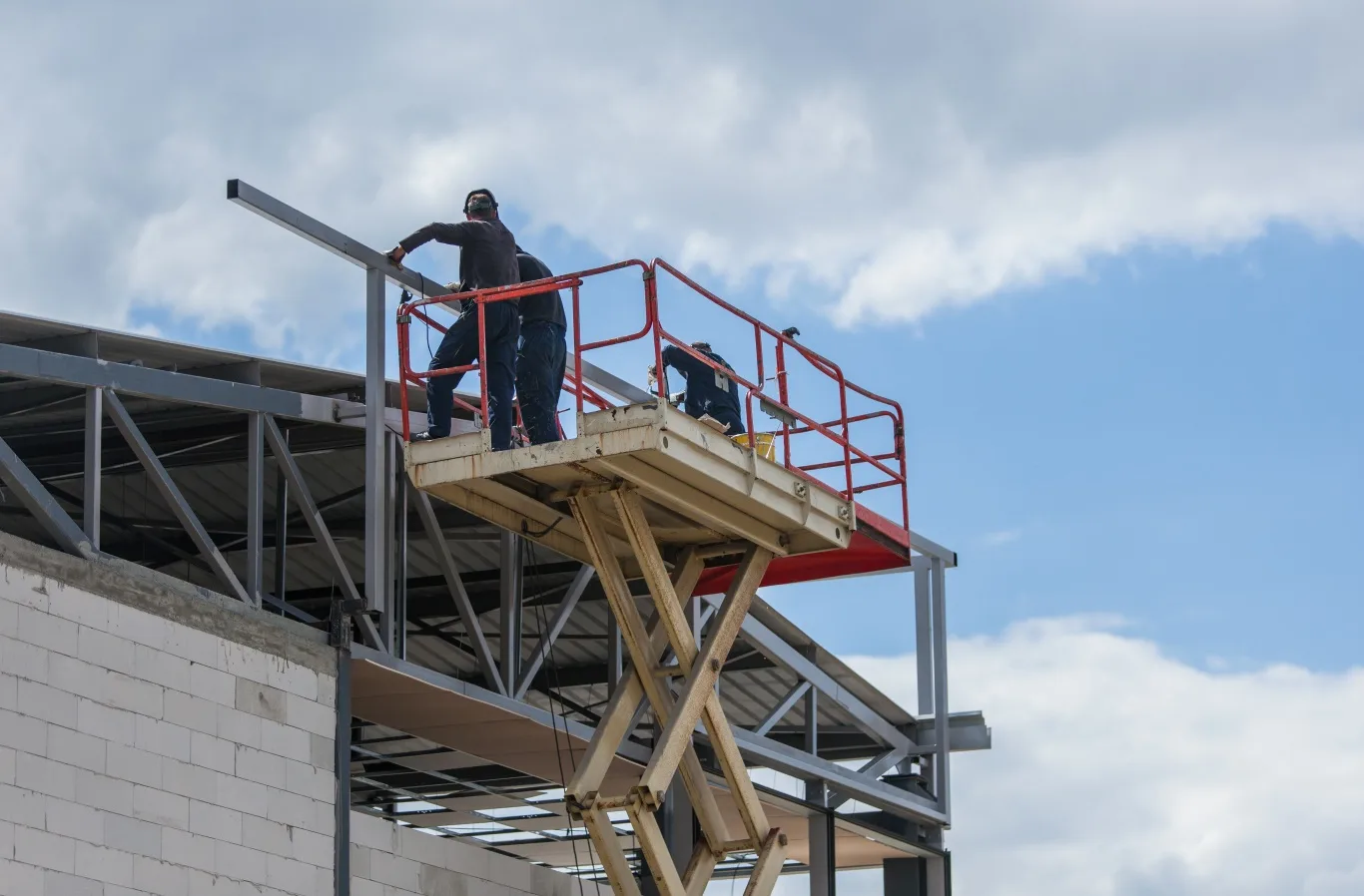Workers using a 25ft scissor lift rental to safely perform construction work on a steel structure under a clear sky in Seattle, Washington.
