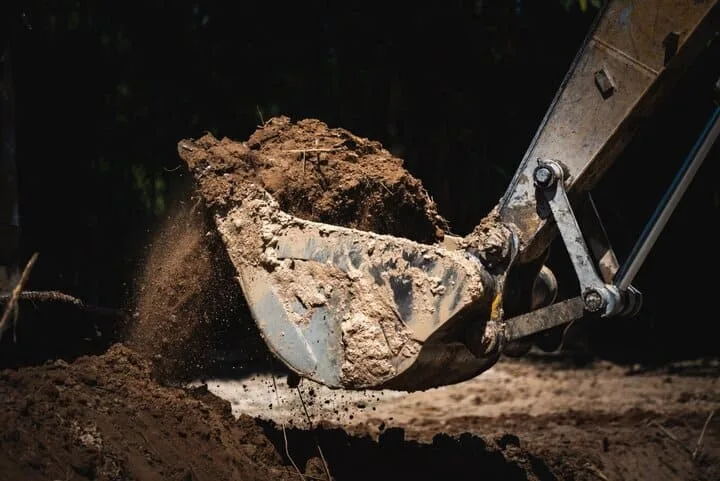 A close-up view of cat excavator buckets scooping soil on a construction site.