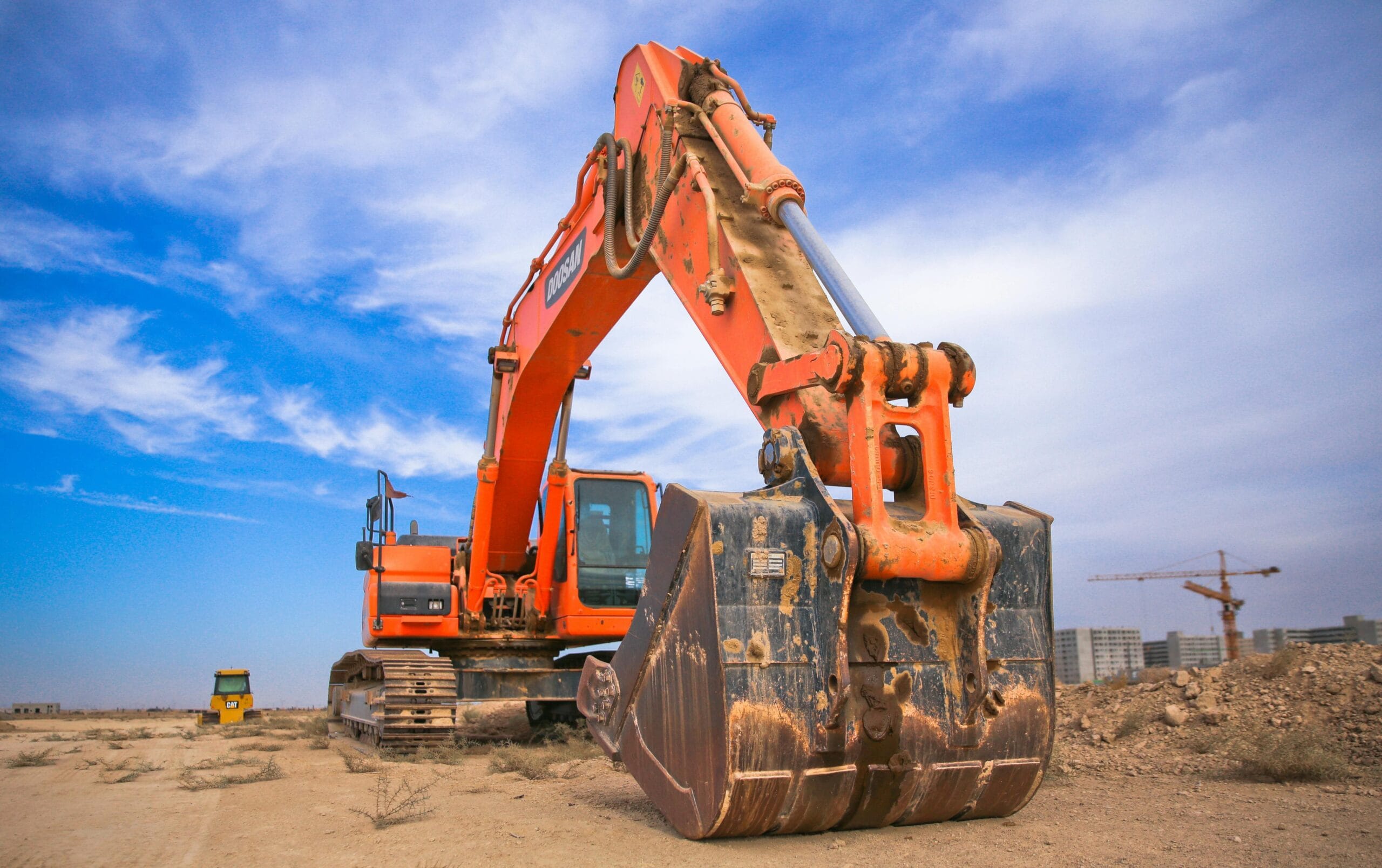 Heavy-duty rental mini excavator on a construction site, positioned for digging and earthmoving work with a large bucket under a clear blue sky.