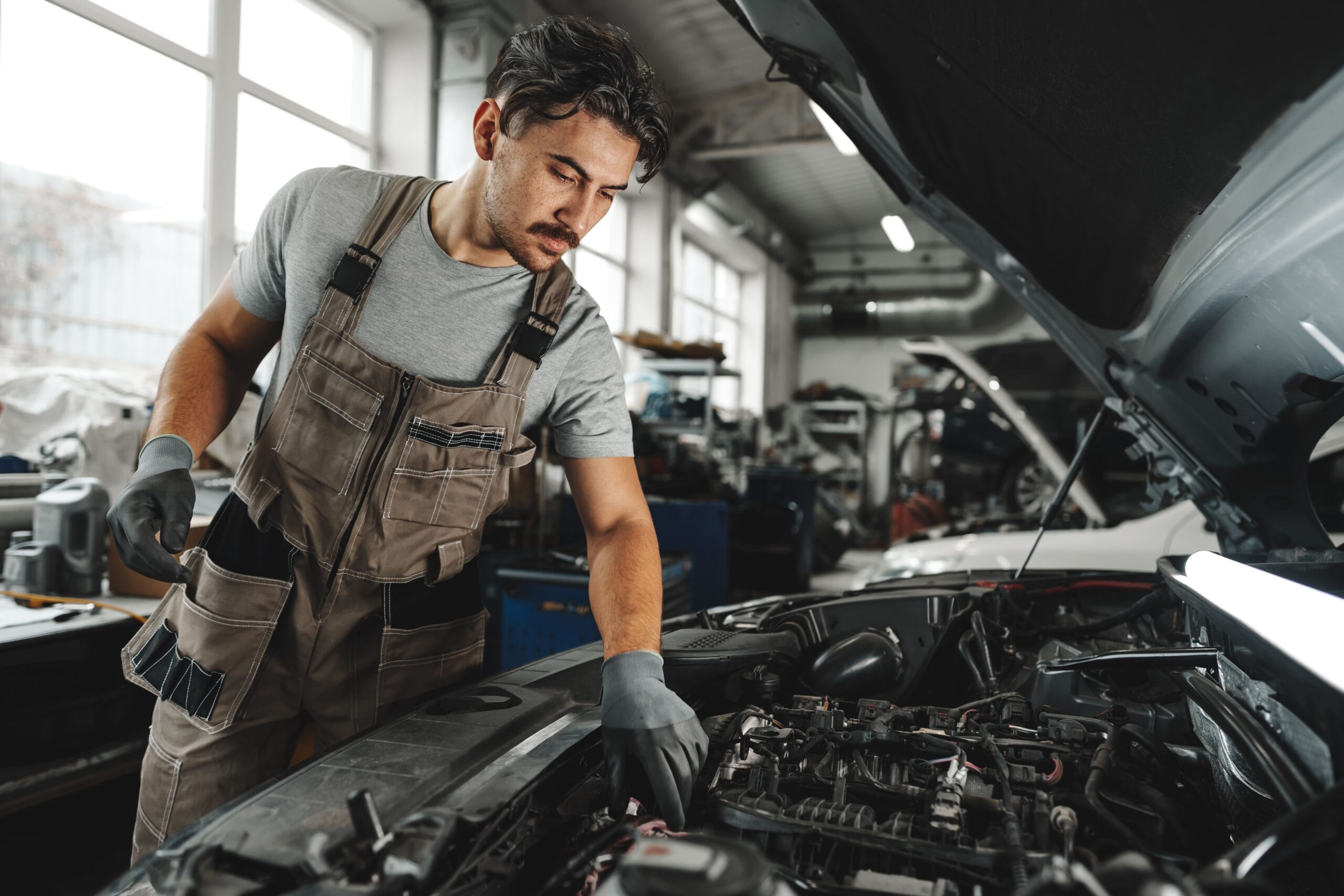 A focused automotive and diesel mechanic at Williams Diesel LLC in Seattle wearing coveralls and protective gloves inspects the complex engine components of a vehicle with the hood raised.