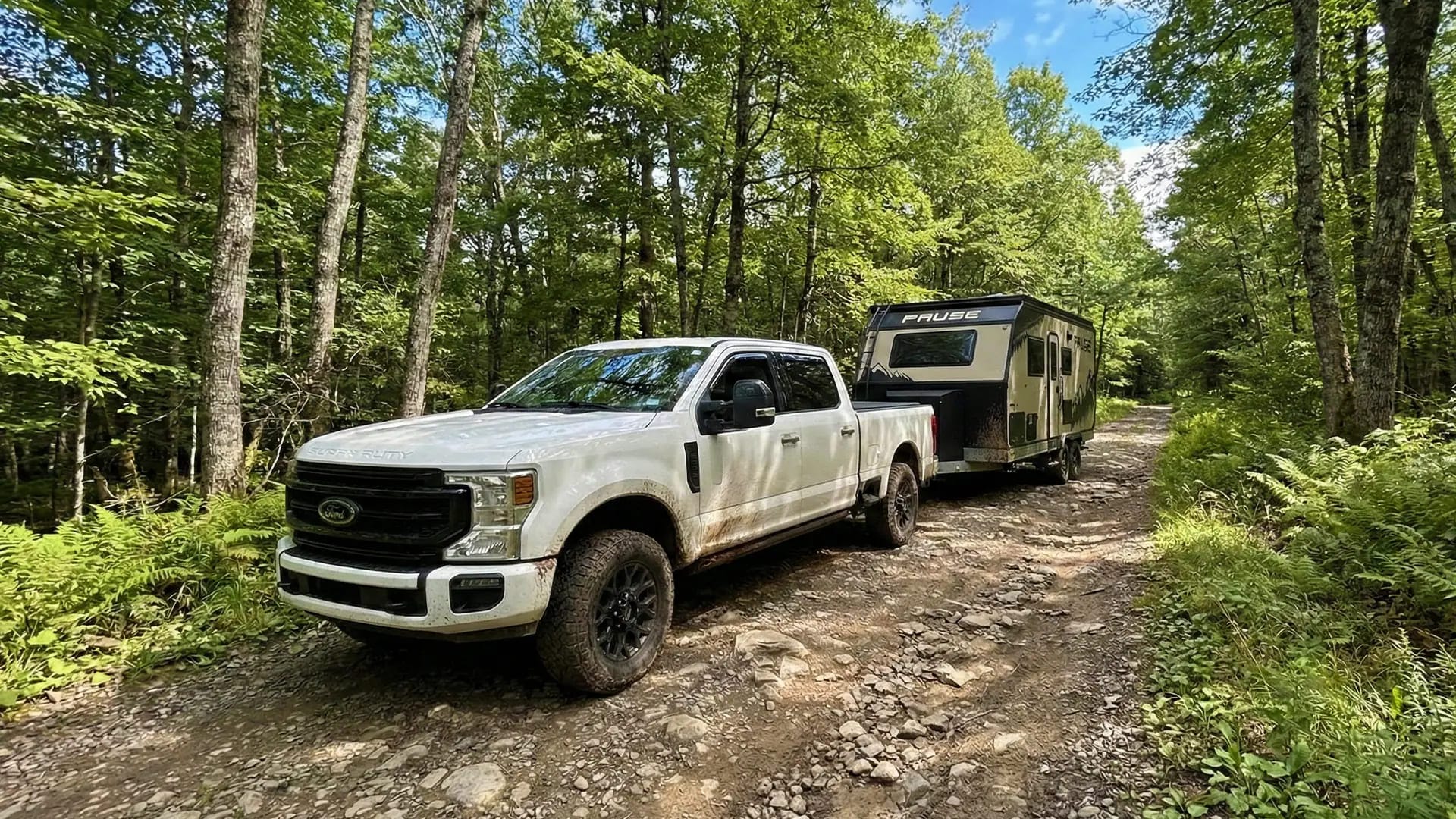 White pickup truck towing a travel trailer on a forest trail, showcasing a reliable Ford F-350 for Rent Washington option for heavy-duty hauling and outdoor travel.