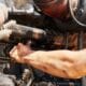 A heavy-duty technician performing systematic troubleshooting and component cleaning for small diesel engine repair on a compact utility powertrain inside a service center.