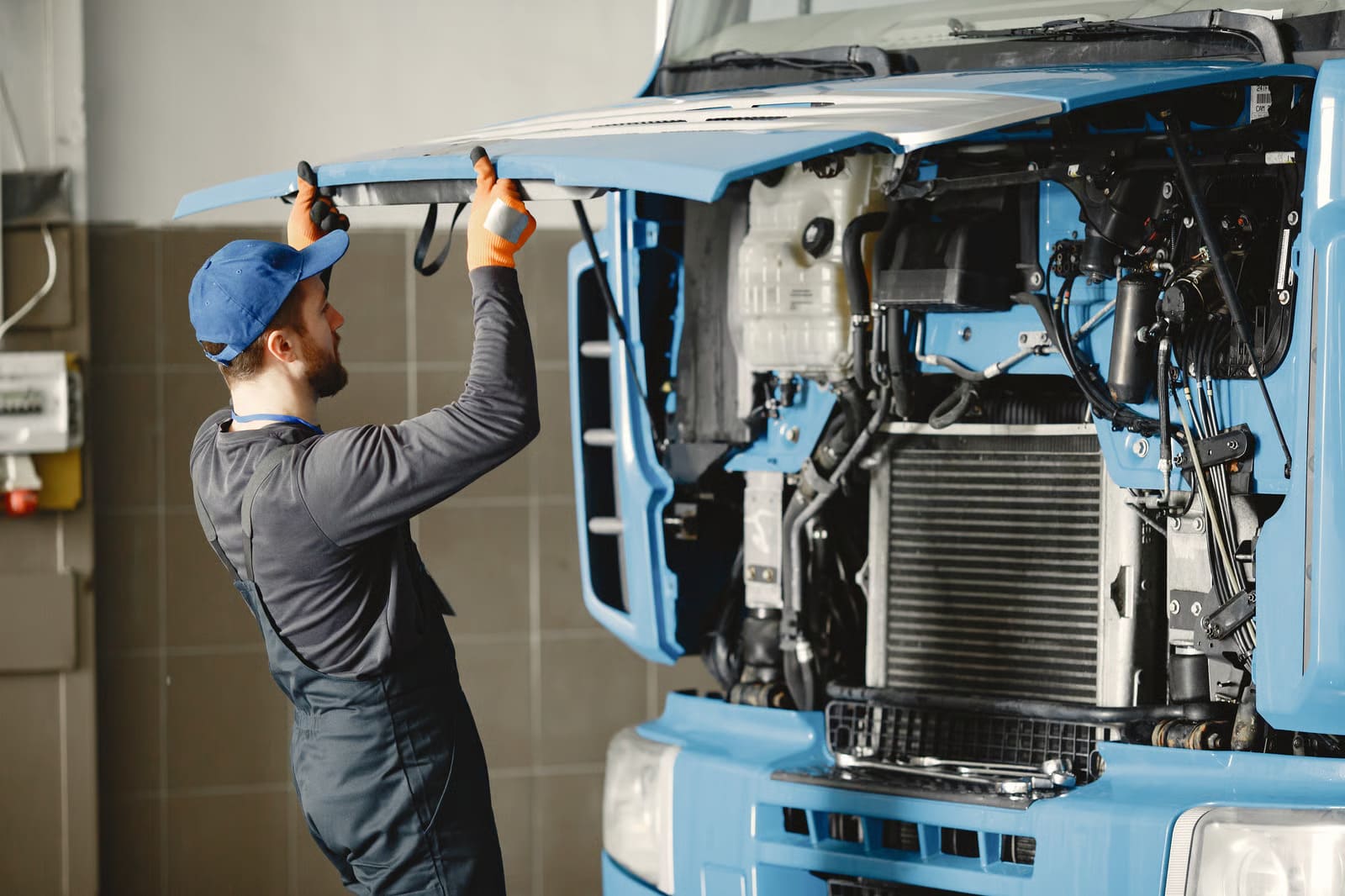 Professional heavy truck mechanics inside a high-clearance commercial bay executing detailed inspections on a large over-the-road diesel transport vehicle.