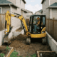 A compact yellow mini excavator working next to a suburban house foundation, demonstrating how the specific caterpillar 303 weight balances heavy breakout force with a turf-friendly layout to prevent structural property damage.
