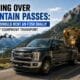 A heavy-duty truck from a rent f350 dually fleet hauling a flatbed gooseneck trailer loaded with an excavator over a scenic mountain highway pass.