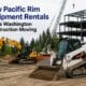 A line of yellow heavy construction machinery including excavators and loaders provided by pacific rim equipment rentals operating on a muddy Seattle job site with the cityscape in the background.